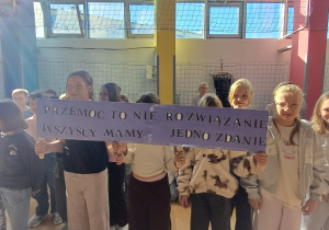 Uczniowie klasy 4d podczas apelu prezentują swoje hasło – „Przemoc to nie rozwiązanie, wszyscy mamy jedno zdanie”.