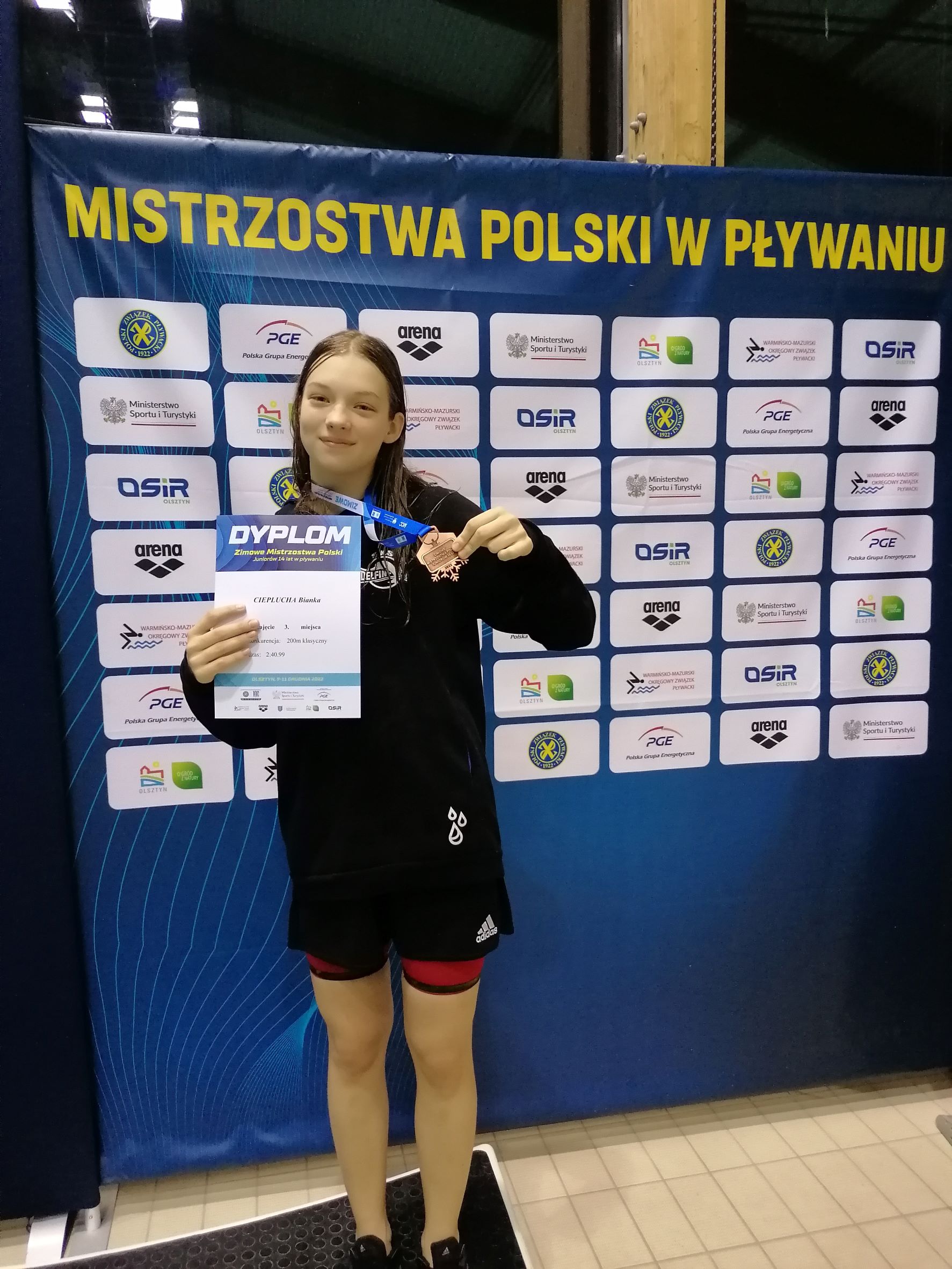 Zawodniczka Bianka Cieplucha trzyma w dłoni brązowy medal zdobyty na Zimowych Mistrzostwach Polski Juniorów młodszych w pływaniu
