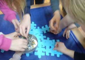 Grupa uczniów przypina do tablicy puzzle w kolorze niebieskim