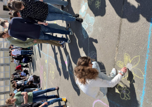Uczennica z klasy 8d wykonuje barwny rysunek kredą na boisku szkolnym z okazji Dnia Ziemi.