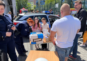 Policyjne stanowisko – radiowóz, policjanci z broszurami i odblaskami