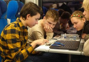 Szymon, Natalia, Franciszek, Michał podczas jazdy pociągiem na ogólnopolski konkurs HackEdu montują robota z elementów Arduino Starter Kit.