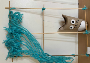 Okienko z patyczków szaszłykowych z doczepioną figurką kota z rolki papierowej i włóczki w kolorze niebieskim