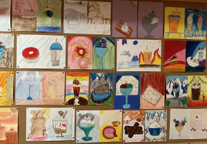 Prace na tablicy szkolnej wykonane przez uczniów klas czwartych w technice pastelowe.j Przedstawiają ulubione desery w barwach ciepłych i zimnych