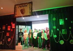 Uczniowie klasy 2a śpiewają kolędę – „Do szopy”, na kotarach kserokopie okładek książek o Mikołaju wydawnictwa Świetlik, u góry napis - Frajda Teatr Szkolny.