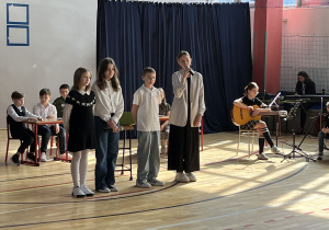 Grupa uczniów z klasy 5 podczas występu na uroczystym apelu z okazji Dnia Patrona