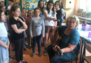Zabawy ze śpiewem na szkolnym korytarzu. Wspólne śpiewanie piosenek. Nauczyciele grają na gitarze.