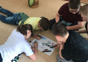 Grupa uczniów z klasy piątej wykonuje zadanie plastyczne na podłodze z zastosowaniem mazaków
