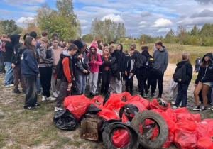 Uczniowie znajdują się na miejscu zbiórki. Na pierwszym planie widoczne worki ze śmieciami zebranymi podczas akcji Sprzątania Świata