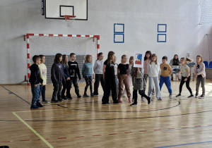 Uczniowie prezentując duży obrazek odznaki zuchowej śpiewają piosenkę „Znaczek zucha”.