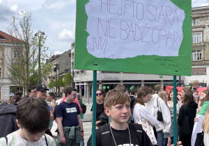 Uczniowie z klasy siódmej stoją na Placu Wolności z przygotowanym transparentem.
