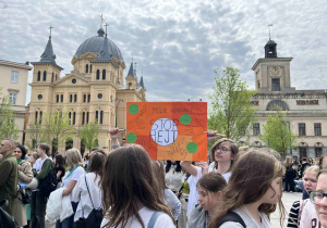 Uczniowie z klasy siódmej stoją na Placu Wolności z przygotowanym transparentem.