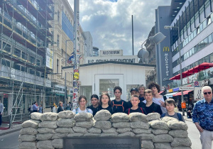 Grupa uczniów stoi przy Legendarnym przejściu granicznym Checkpoint Charlie w Berlinie