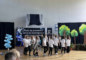 Część artystyczna Jubileuszu – występ uczniów. W tle dekoracja nawiązująca do historii szkoły i postaci patrona Aleksandra Kamińskiego