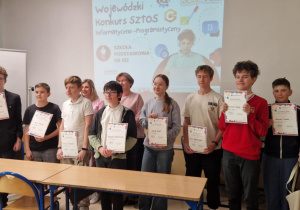 Zdjęcie grupowe uczestników konkursu informatycznego z dyplomami i nagrodami.