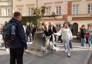 Grupa uczniów chodzi wokół dzwonu na placu Kanonia