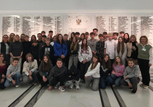 Uczestnicy wycieczki stoją w holu głównym budynku Sejmu pod tablicą upamiętniającą parlamentarzystów poległych w czasie II wojny światowej.