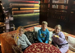 Dzieci siedzą przy stole nakrytym obrusem, czekając na zajęcia.