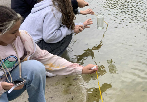 Uczennice mierzą temperaturę wody w zbiorniku.