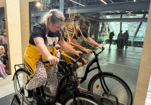 Uczennica na rowerku stacjonarnym sprawdza jak można wyprodukować energię.