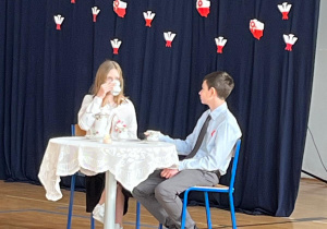 Uczniowie z klasy 8b i 8d siedzą przy okrągłym stole, prowadzą uroczystość