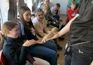 Pracownik pokazuje uczniom jaszczurkę agamę.