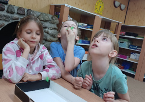 Ćwiczenia oddechowe z piórkami, dziewczynki starają się zdmuchnąć piórka do pudełka.