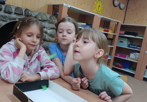 Ćwiczenia oddechowe z piórkami, dziewczynki starają się zdmuchnąć piórka do pudełka.