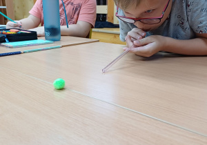 Uczniowie wykonują ćwiczenia oddechowe – „strzelają gole” dmuchając przez słomkę na piłeczkę.