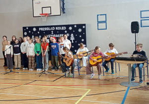 Dzieci z klasy 5d śpiewają i grają na instrumentach muzycznych kolędę – „Przybieżeli do Betlejem”.