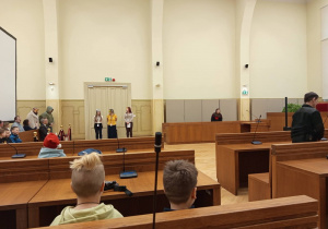 Dzieci przyglądają się pozorowanej rozprawie sądowej, w której pracownicy sądu wcielają się w zwierzęta.