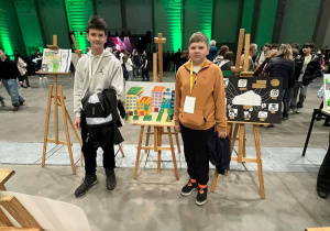 Uczniowie z klasy 7a stoją przy swojej pracy konkursowej zaprezentowanej w hali EXPO.