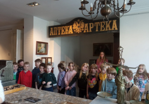 Uczniowie stoją na na tle starego napisu apteka, z czasów, gdy Łódź była w zaborze rosyjskim.