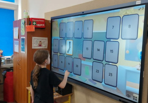 Uczennica klasy pierwszej rozwiązuje zadanie typu memory na tablicy multimedialnej.