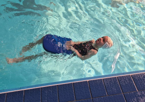 Zawodnik płynie w sztafecie stylem grzbietowym