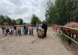 Pierwszaki stoją w rzędzie czekając na to żeby mogły nakarmić trawą konie.