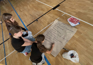 Uczniowie z klas 4 – 5 w trakcie apelu na dużym formacie papieru zapisują hasła przeciwko przemocy rówieśniczej
