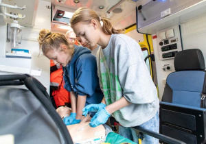 Reanimacja w karetce pogotowia Prowadzona przez Martynę, Maja podłącza poszkodowanemu elektrody AED.
