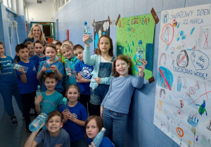Klasa 2a prezentuje radośnie plakaty z okazji Dnia Święta Wody zamieszczone przed szkolną pływalnią