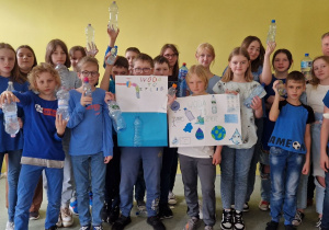 5b z wychowawcą prezentuje kilka plakatów przygotowanych z okazji Dnia Wody. Uczestnicy prezentacji trzymają w dłoniach butelki z wodą.