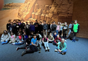 Zdjęcie grupowe uczestników wycieczki w Muzeum Nowa Praga na tle fototapety przedstawiającej malowniczą Dolinę Królów w Luksorze