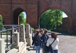 Uczniowie z przewodnikiem zwiedzają Toruń, przechodzą przez Bramę Miasta