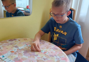 Zajęcia logopedyczne - uczeń gra w domino logopedyczne, służące utrwalaniu głosek sz, ż/rz, cz, dż.